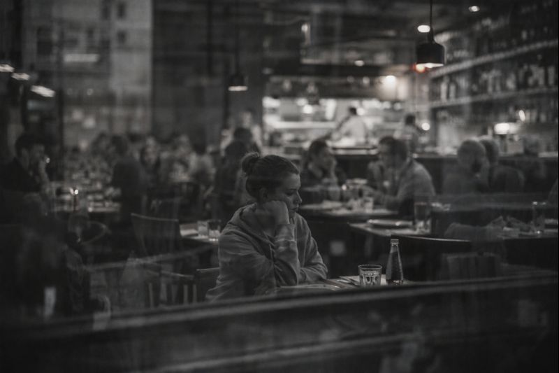 Persoana intr-un restaurant, vazuta prin reflexia unui geam, scena alb-negru