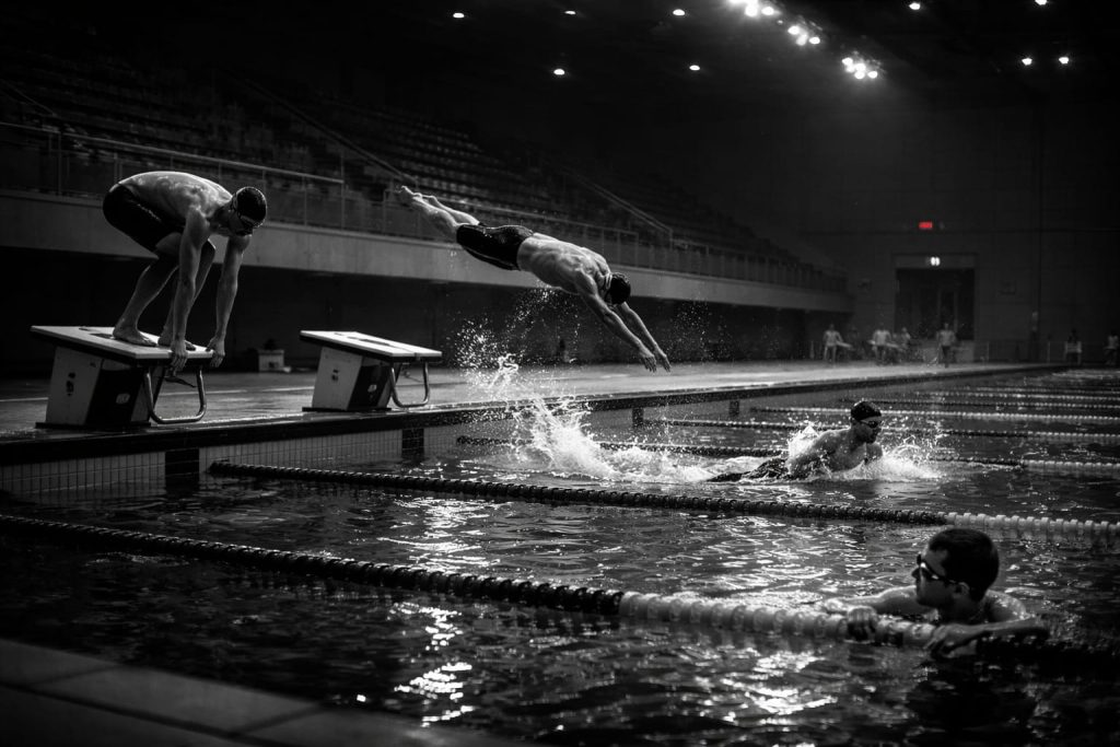 bazin olimpic cu patru inotatori in etape diferite ale unei sarituri, stil ab-negru.